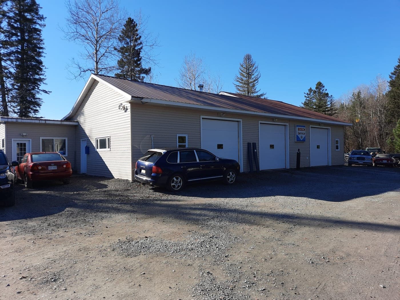 The garage at MacNeil's AutoHaus, bay doors facing a gravel lot with customer vehicles parked alongside